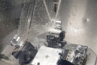 Auf dem Bild ist ein metallverarbeitendes Verfahren mit einer Werkzeugmaschine zu sehen, bei dem Wasser oder Kühlmittel auf ein bearbeitetes Werkstück gesprüht wird.