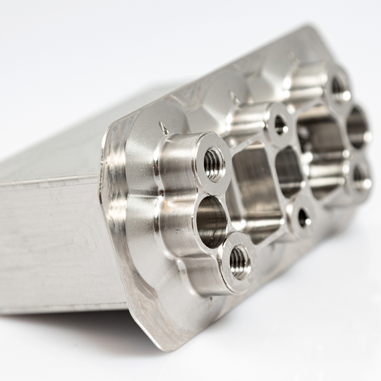 Auf dem Bild ist ein bearbeitetes Metallteil mit mehreren Bohrungen und einer glatten Oberfläche zu sehen.